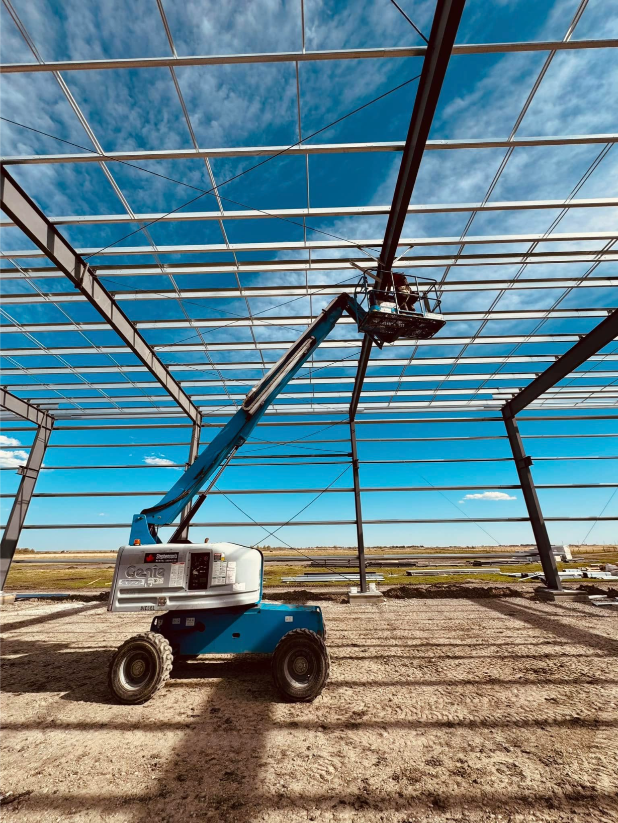 A worker in a lift installs beams under a clear blue sky