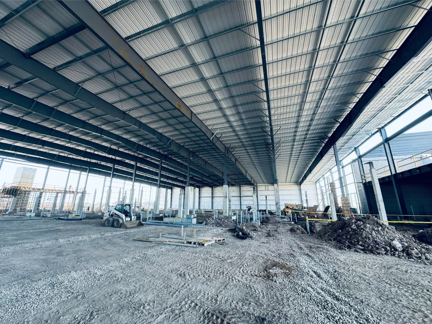 Metal buildings showcase exposed beams and construction equipment in a large industrial space