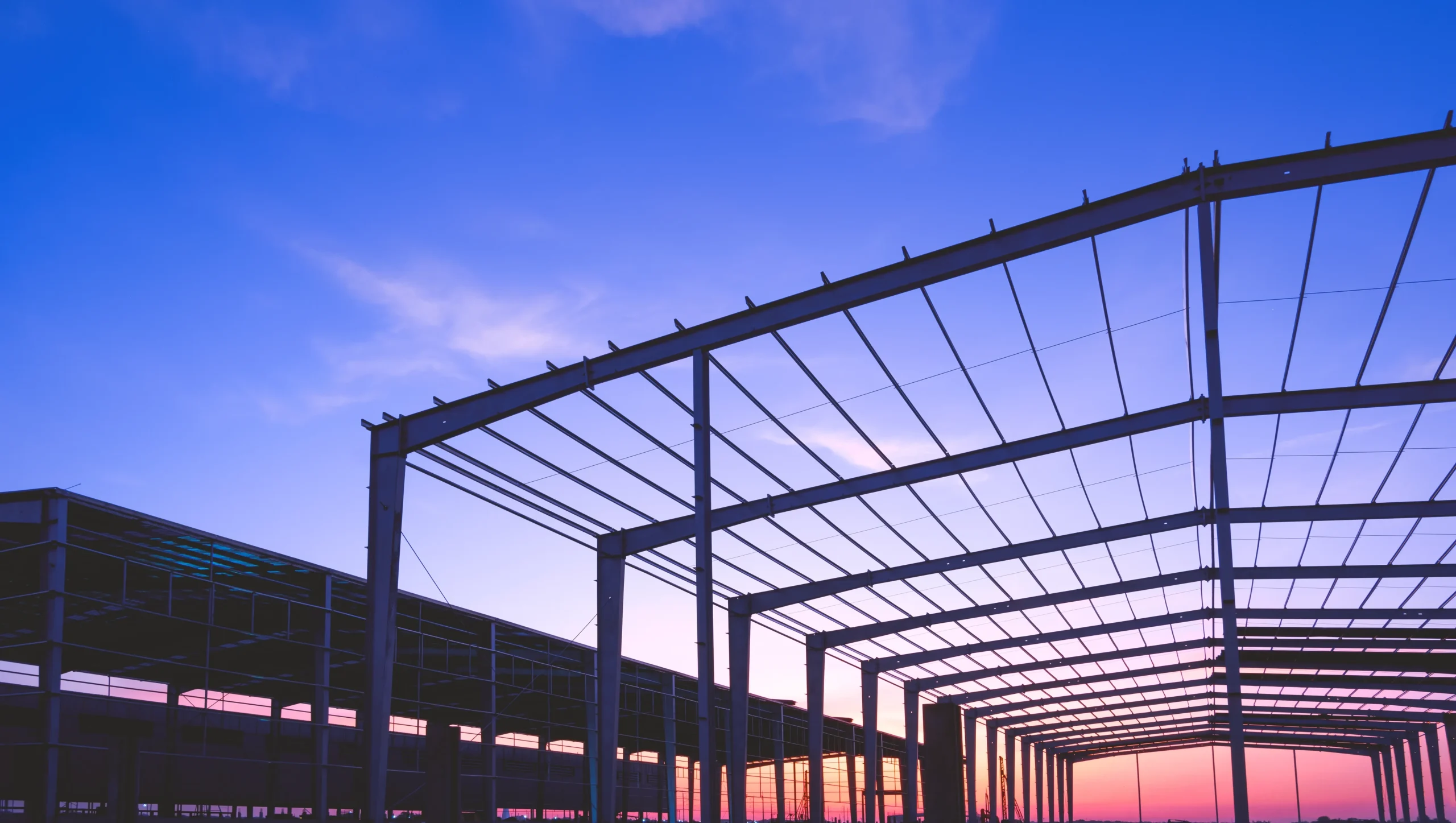 Building envelope defined by structural beams against a vibrant sunset sky